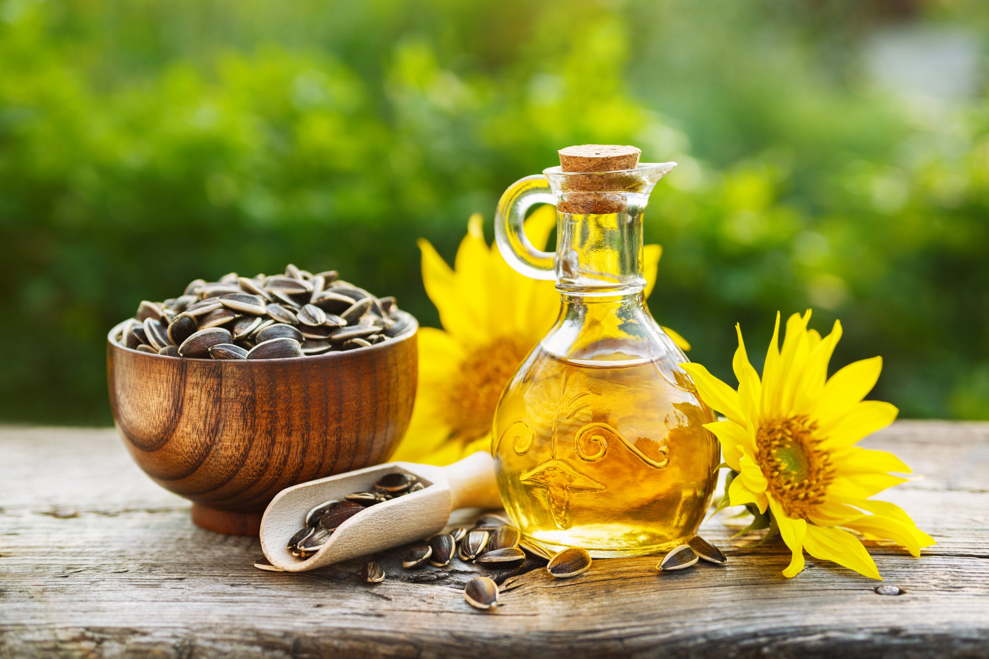 bottle of sunflower oil with vitamin e next to sunflowers and bowl of sunflower seeds